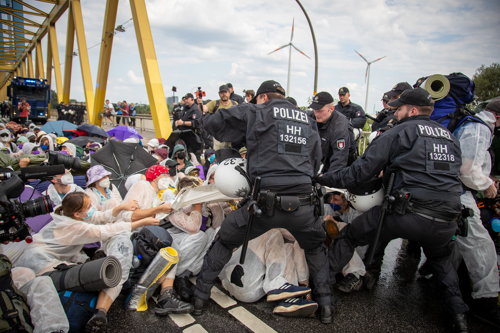Das Bild zeigt Aktivist*innen des Lila Fingers beim besetzen der Kattwykbrücke. Während die Polizei versucht die Aktivist*innen zum Aufgeben zu zwingen.
