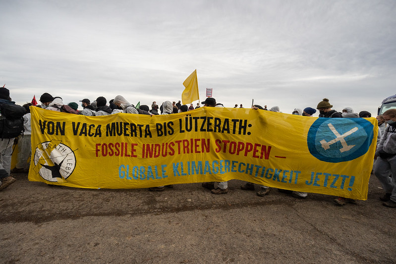 Aktivist*innen tragen ein Banner auf dem steht "Von Vaca Muerta bis Lützerath: Fossile Idustrien stoppen - globale Klimagerechtigkeit jetzt!